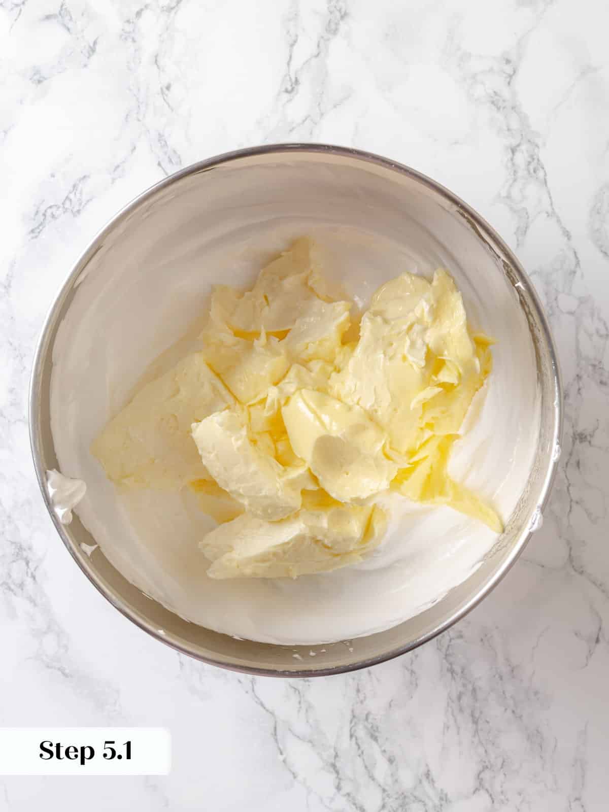 Butter pieces being added into cooled meringue inside a stand mixer bowl.