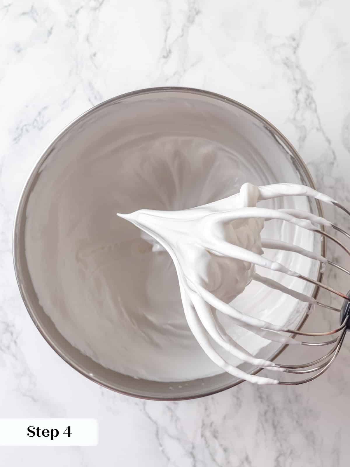 Whipped meringue reaching stiff peaks inside a stand mixer after heating egg whites.