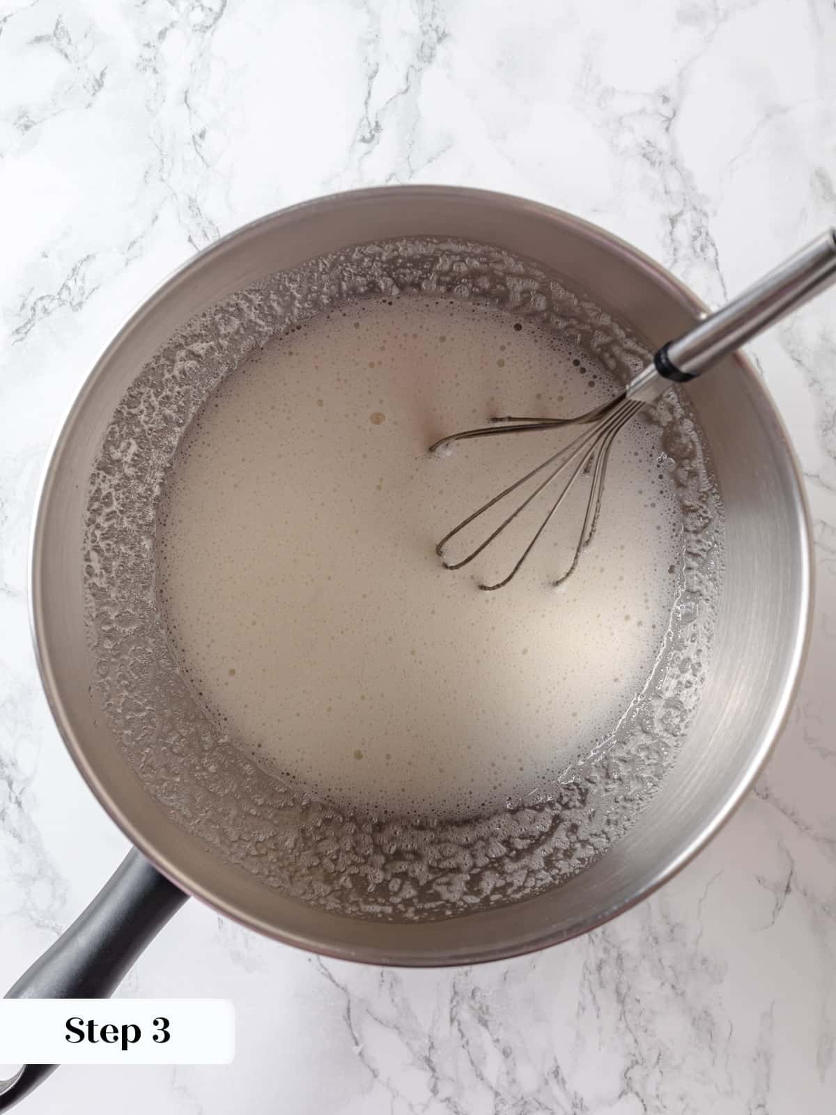 A bowl set over simmering water with egg whites and sugar being cooked until lighter.