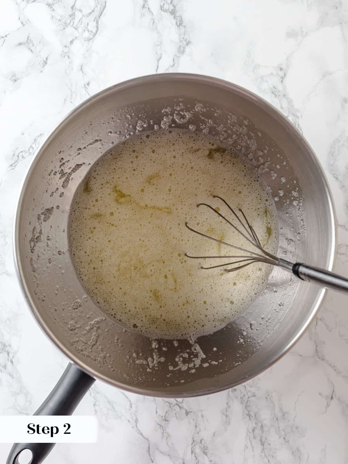 Egg whites and sugar being whisked together in a mixing bowl before heating.