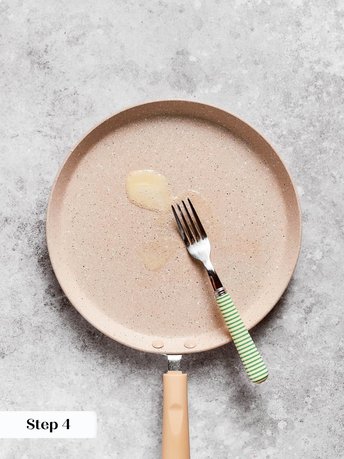 Pan being lightly coated with butter using a fork before pouring the first crepe batter.