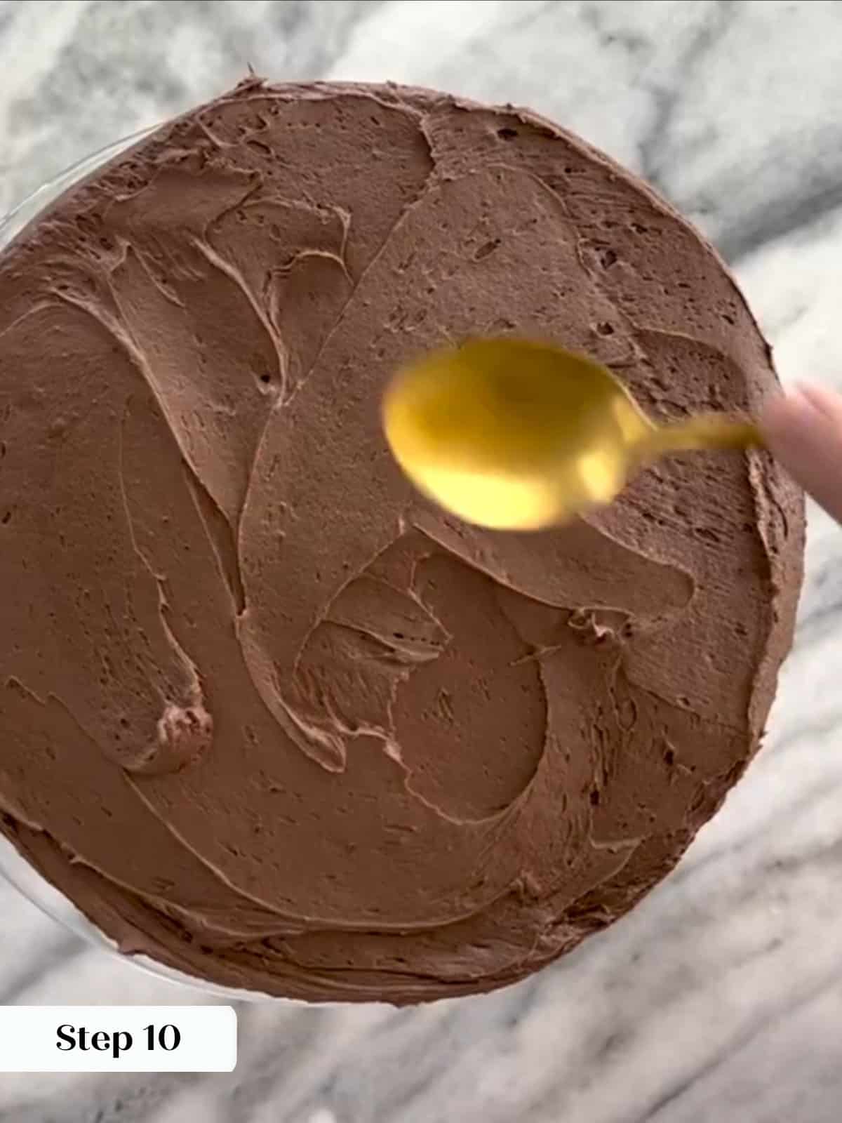 Chocolate buttercream spread smoothly over yellow cake layers using a spoon.