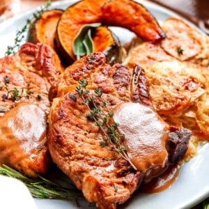 Pork chops coated in applesauce sauce with a fresh thyme sprig on top.