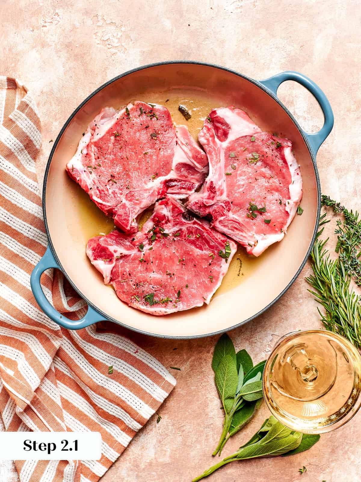 Herb-seasoned pork chops cooking in hot pan during searing step.