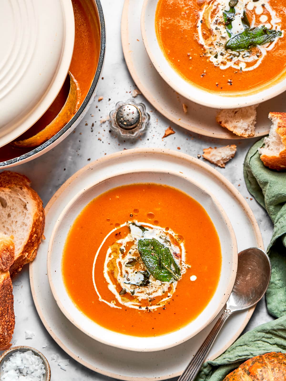 Bright orange vegan pumpkin soup topped with a swirl of coconut cream and a drizzle of oil.