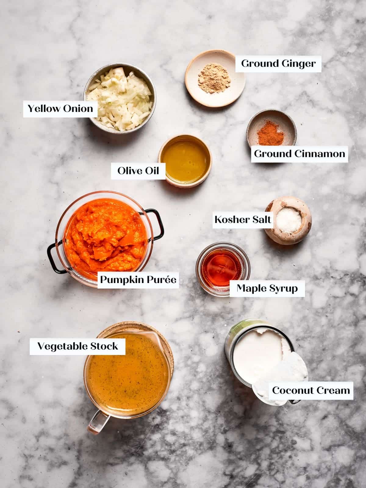 Pumpkin soup ingredients arranged on a countertop including pumpkin puree, coconut cream, onions, and spices.