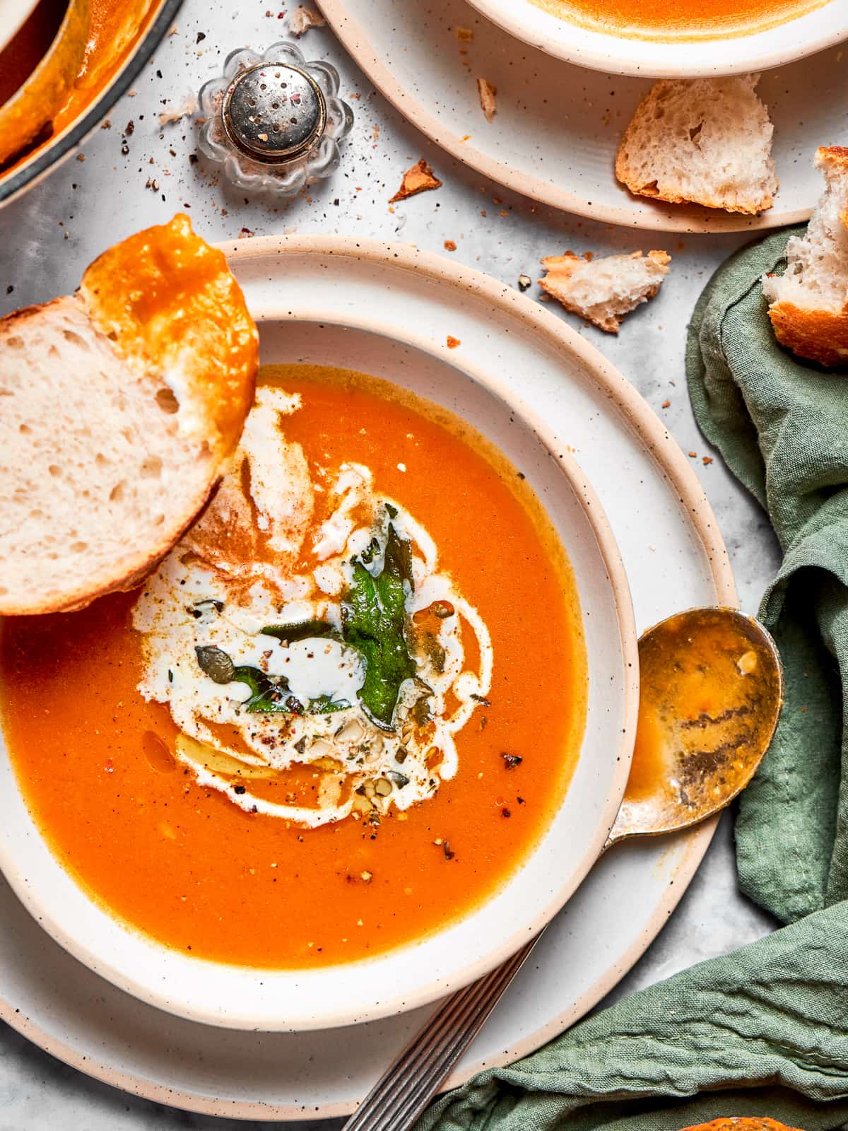Pumpkin soup served in a bowl with soft pieces of torn bread arranged nearby for dipping.