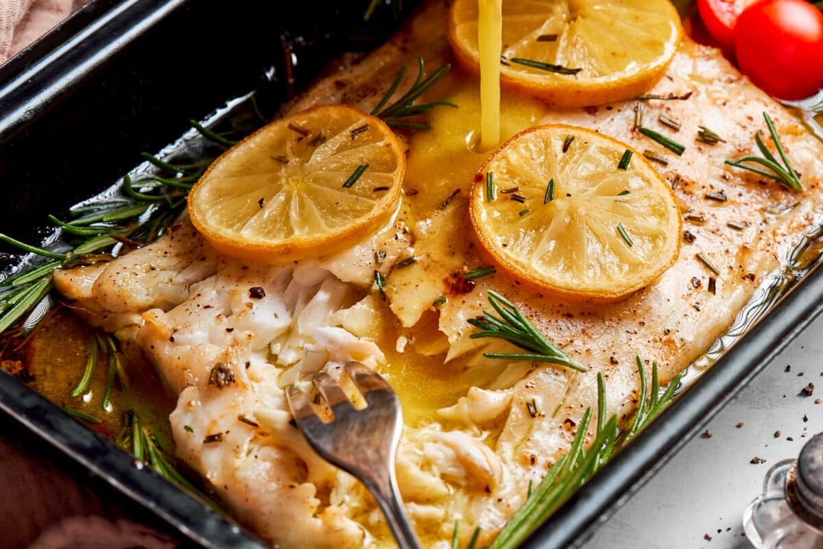 Champagne vinaigrette poured over baked halibut with lemon slices on a pan.