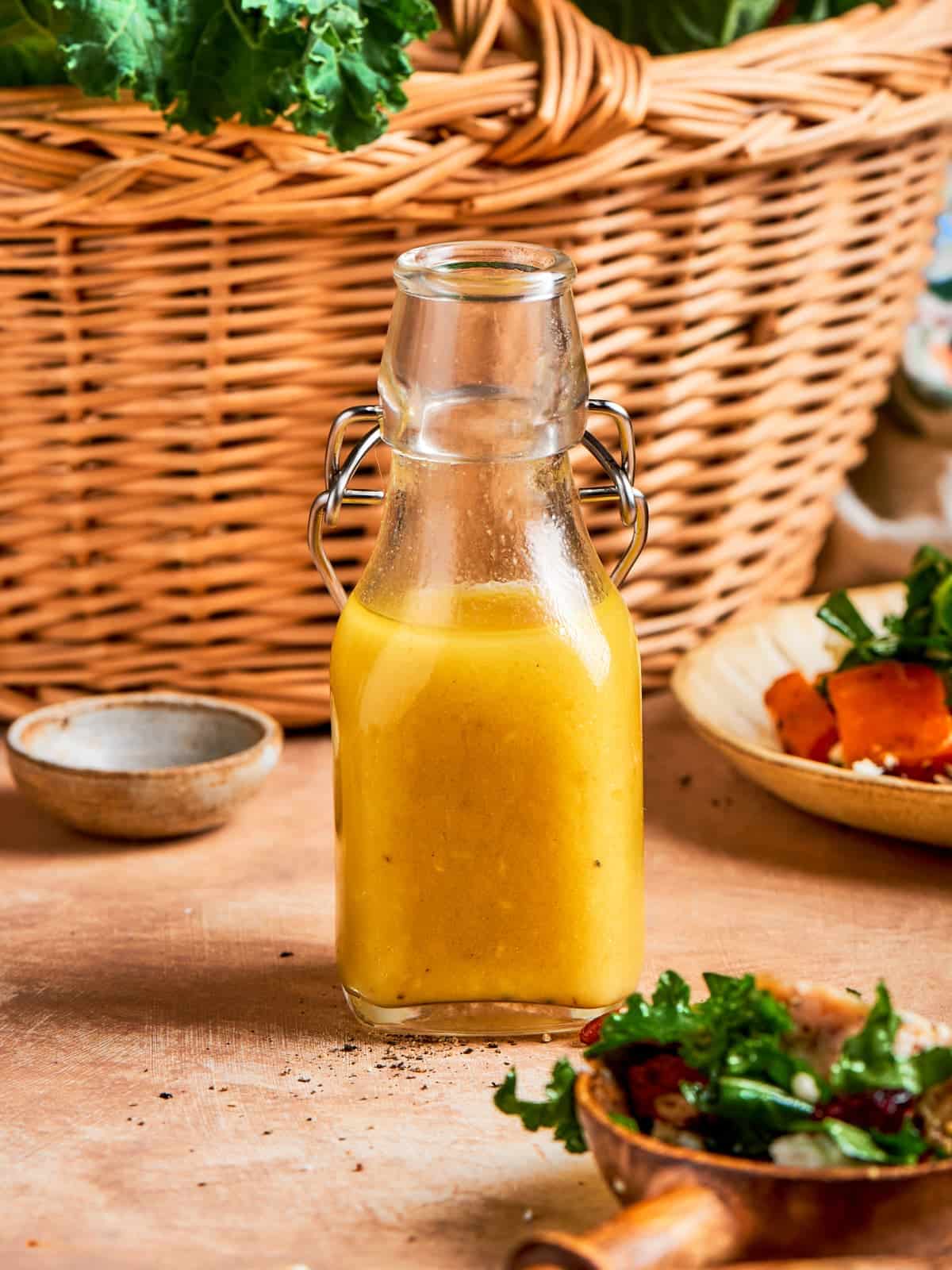 Bottle of homemade champagne vinaigrette standing in front of a woven kitchen basket.