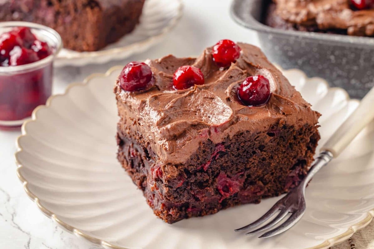 Moist chocolate cherry cake slice showing cherries baked inside and extra cherries on top.