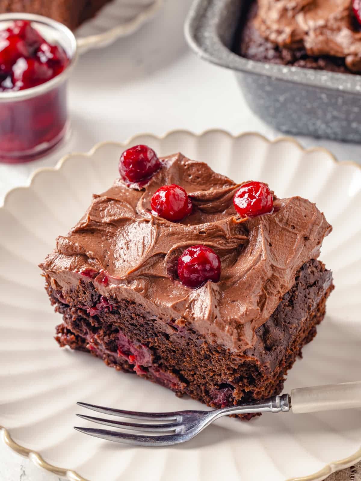 Rich chocolate cake topped with cream cheese frosting resting on a decorative plate.