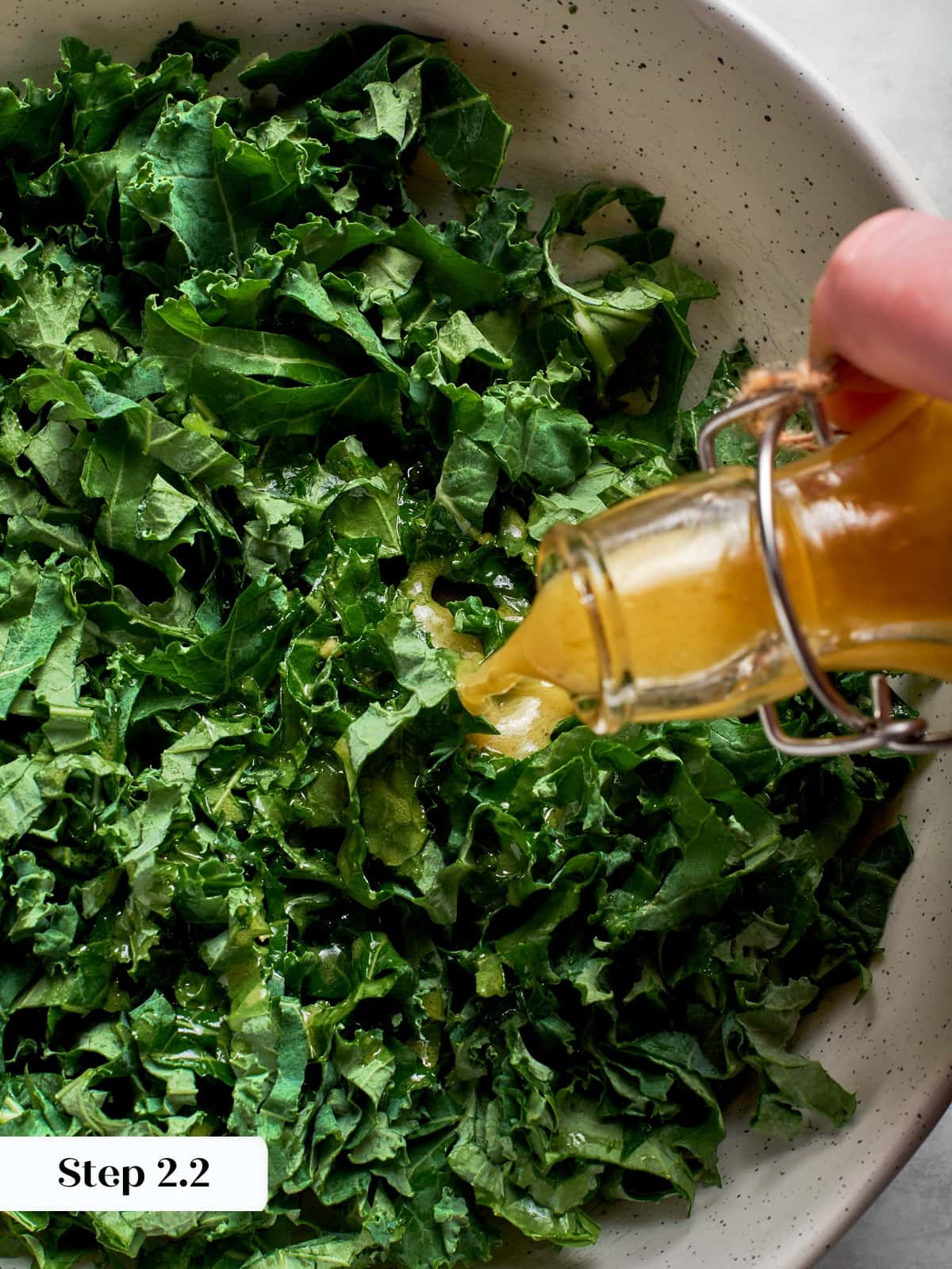 Champagne vinaigrette being added to sliced kale to soften leaves before assembling salad.