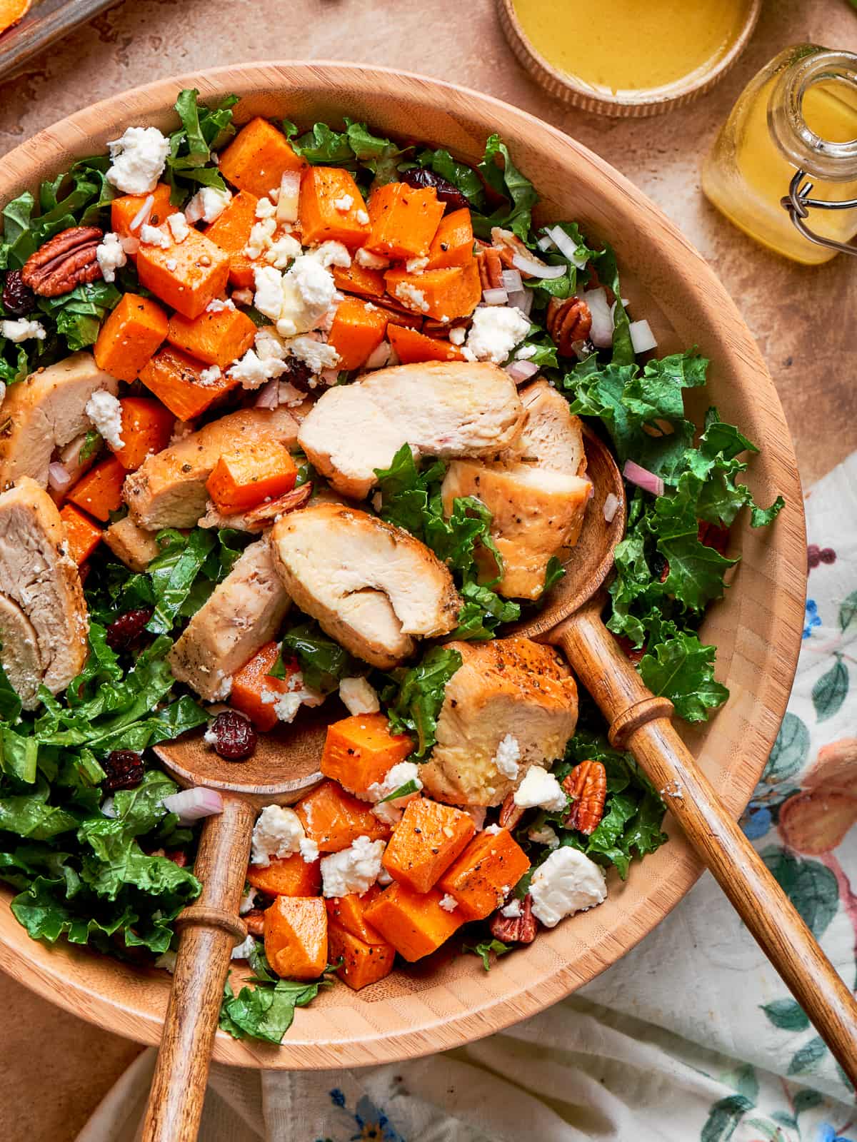 Fully mixed kale sweet potato salad ready to serve with extra dressing nearby.