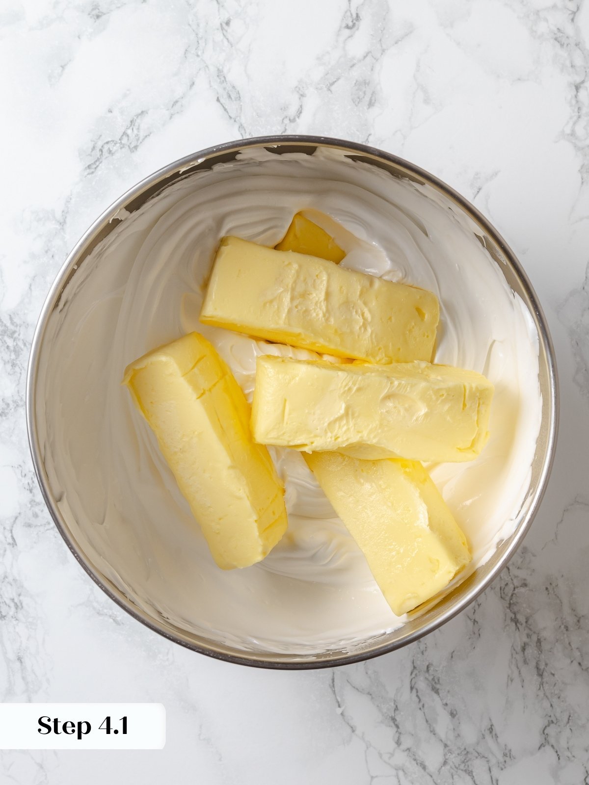 Cubes of butter added to whipped meringue during buttercream preparation.