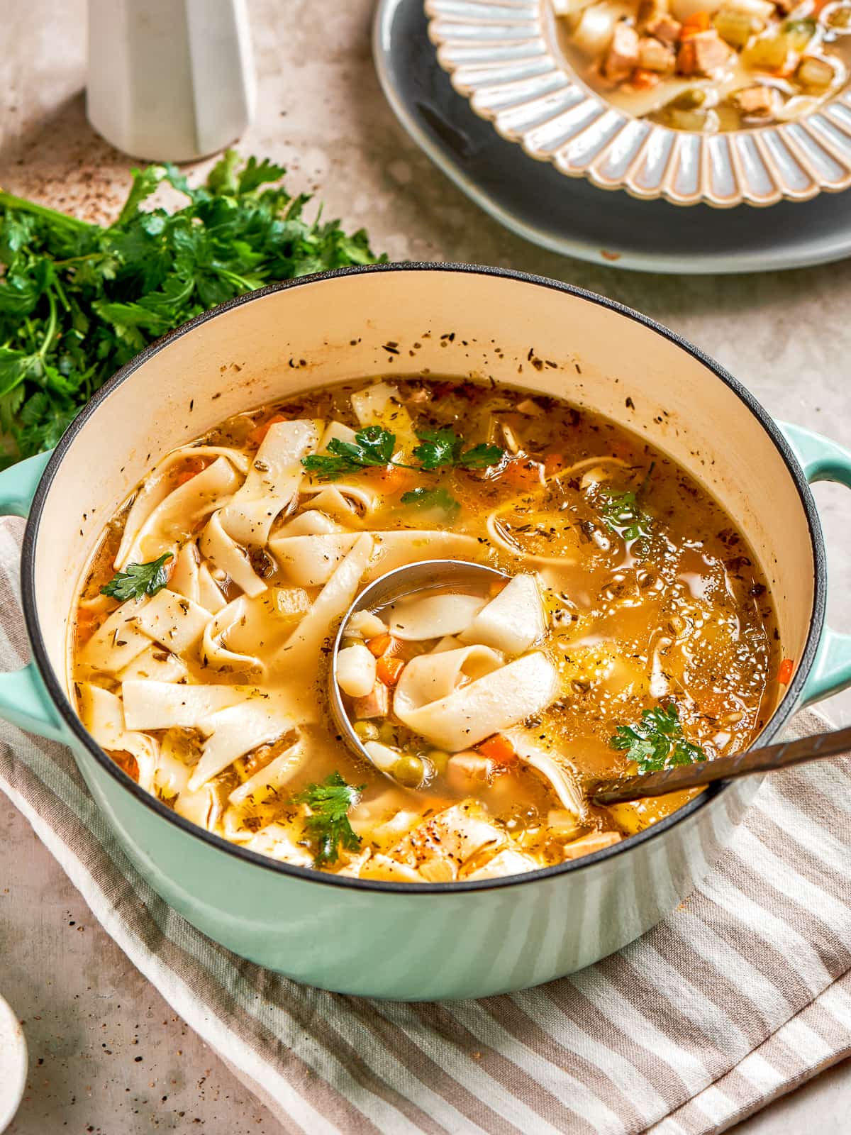 Chicken noodle soup in a blue pot with vegetables and herbs visible.