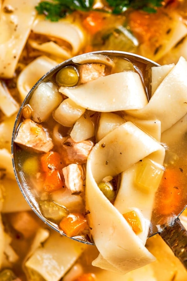 Ladle lifting hearty chicken noodle soup filled with vegetables and noodles.