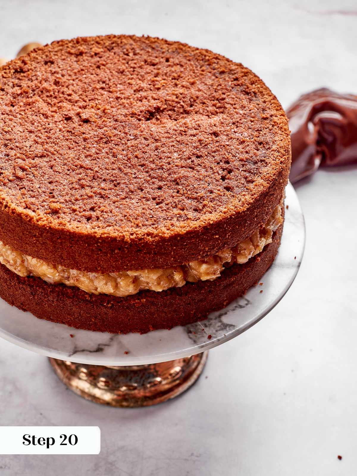 Second chocolate cake layer placed gently on ganache filling and frosting dam.