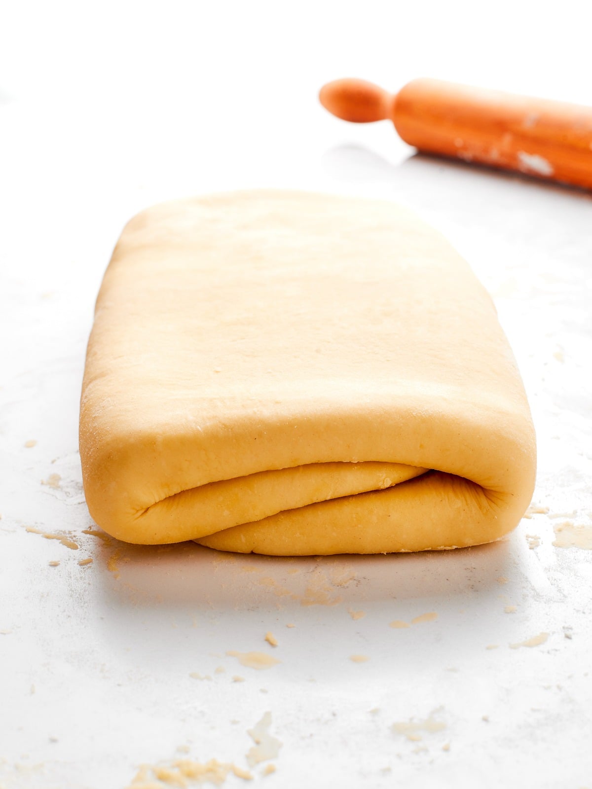 Dough next to rolling pin which will be used to create uniform sheet before folding.