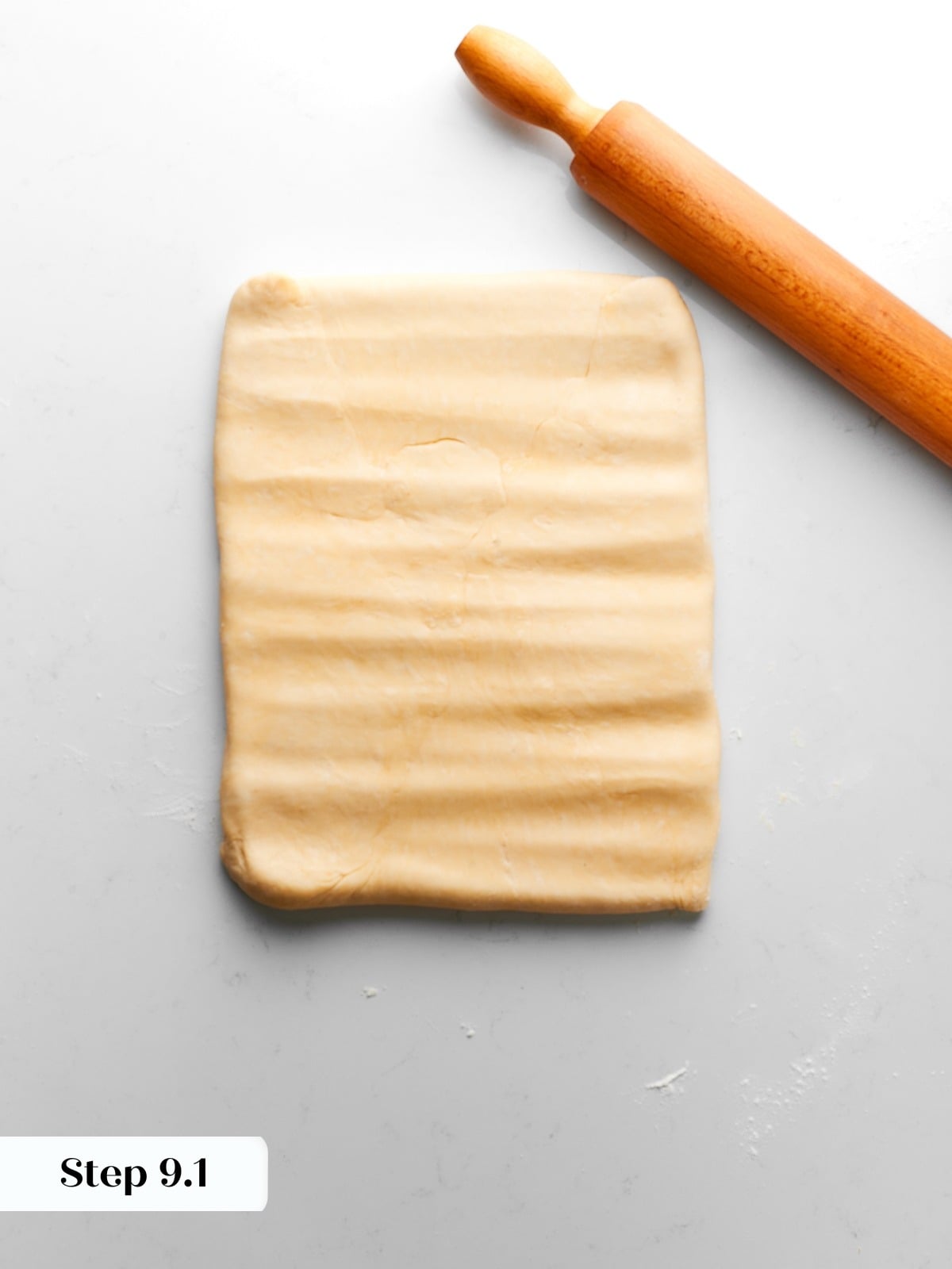 Dough with enclosed butter rolled out carefully to distribute layers evenly throughout pastry.