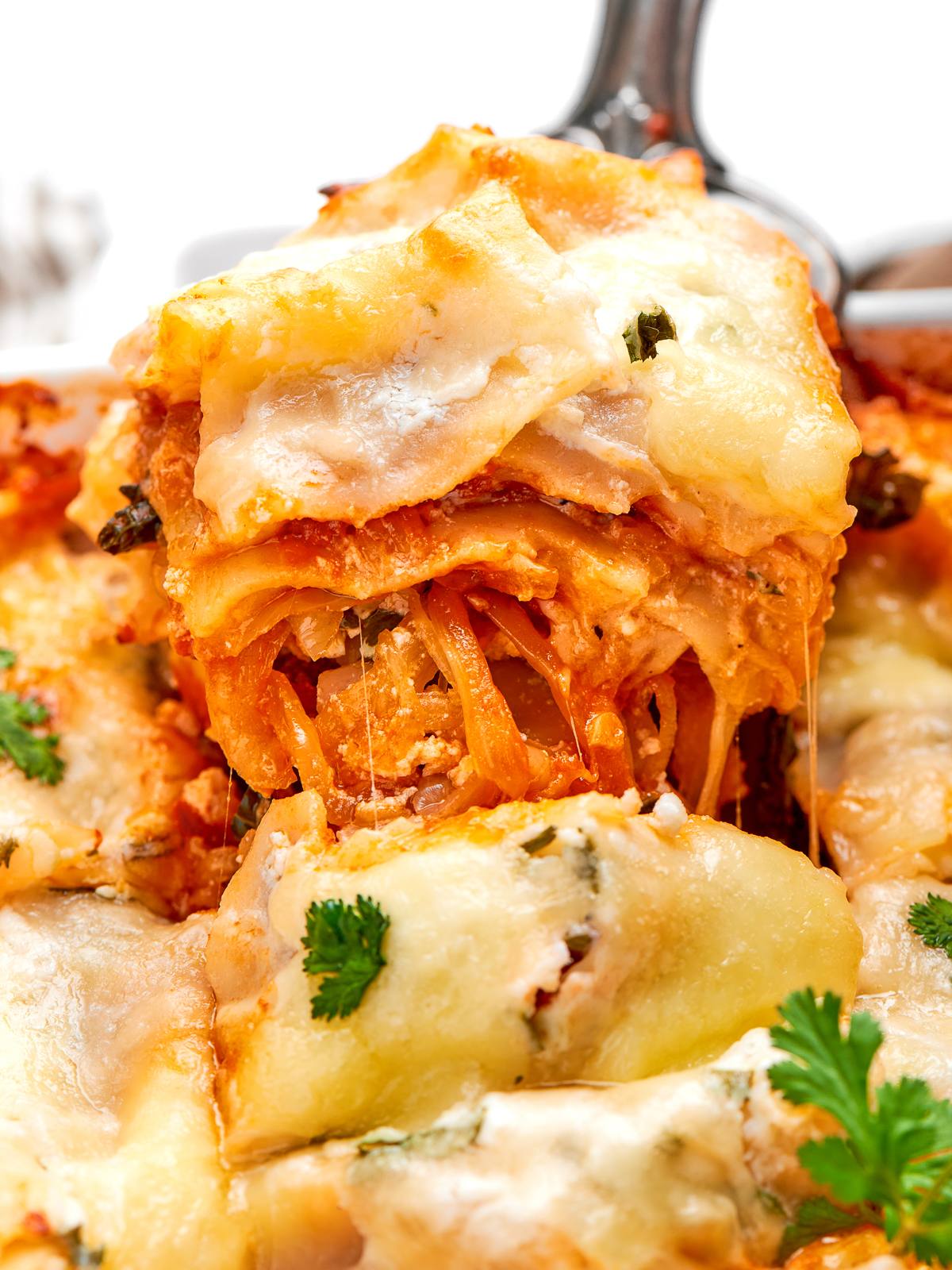 Spaghetti squash lasagna slice lifted with long strands of melted mozzarella stretching from pan.