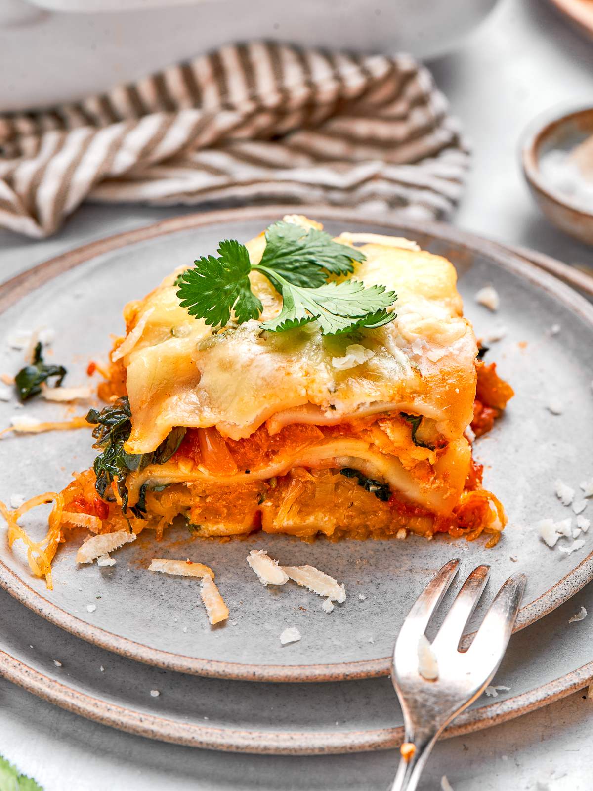 Serving of spaghetti squash lasagna plated on grey dish with melted cheese and herbs.