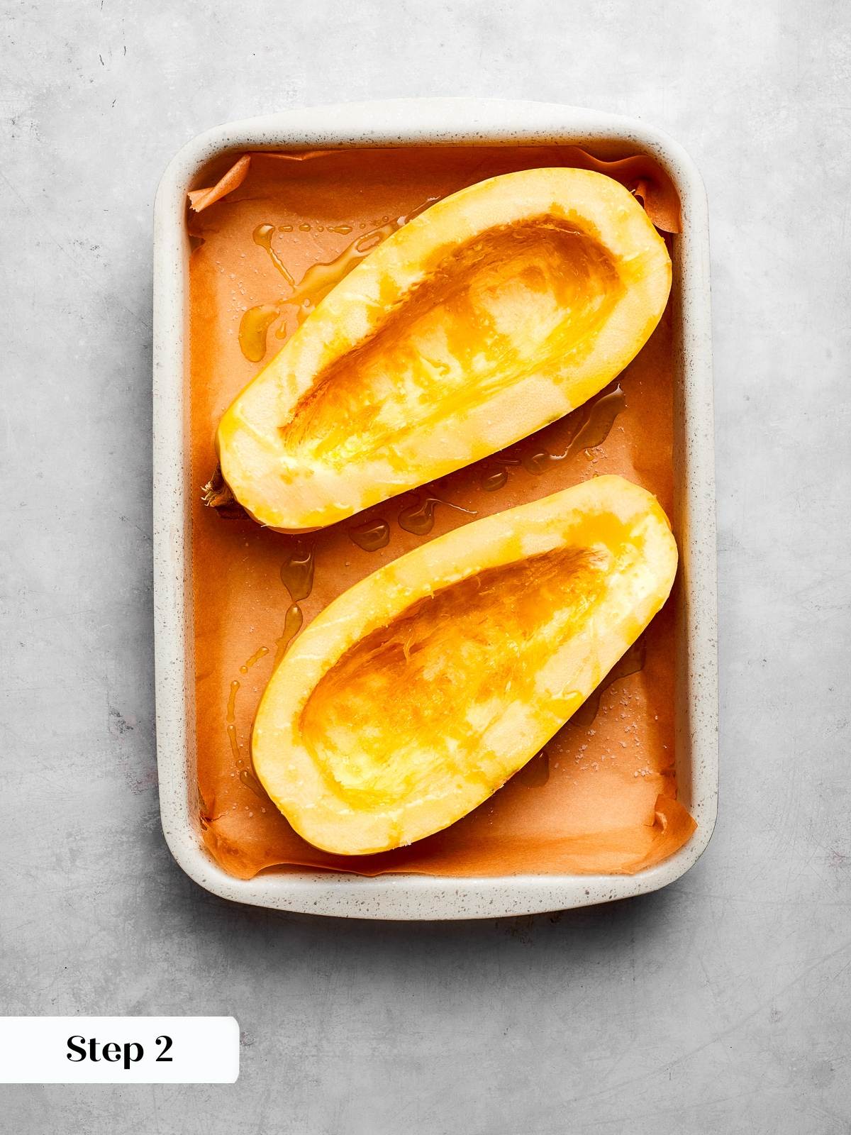 Halved uncooked spaghetti squash on baking sheet ready for roasting and seasoning.