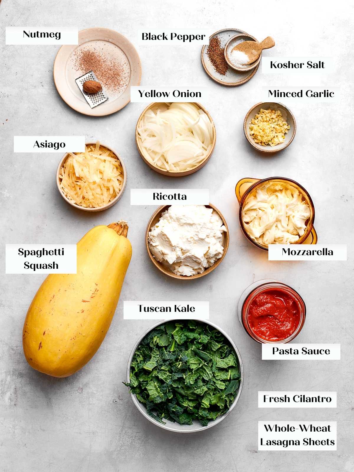 Ingredients for spaghetti squash lasagna arranged on countertop including squash, cheese, and vegetables.