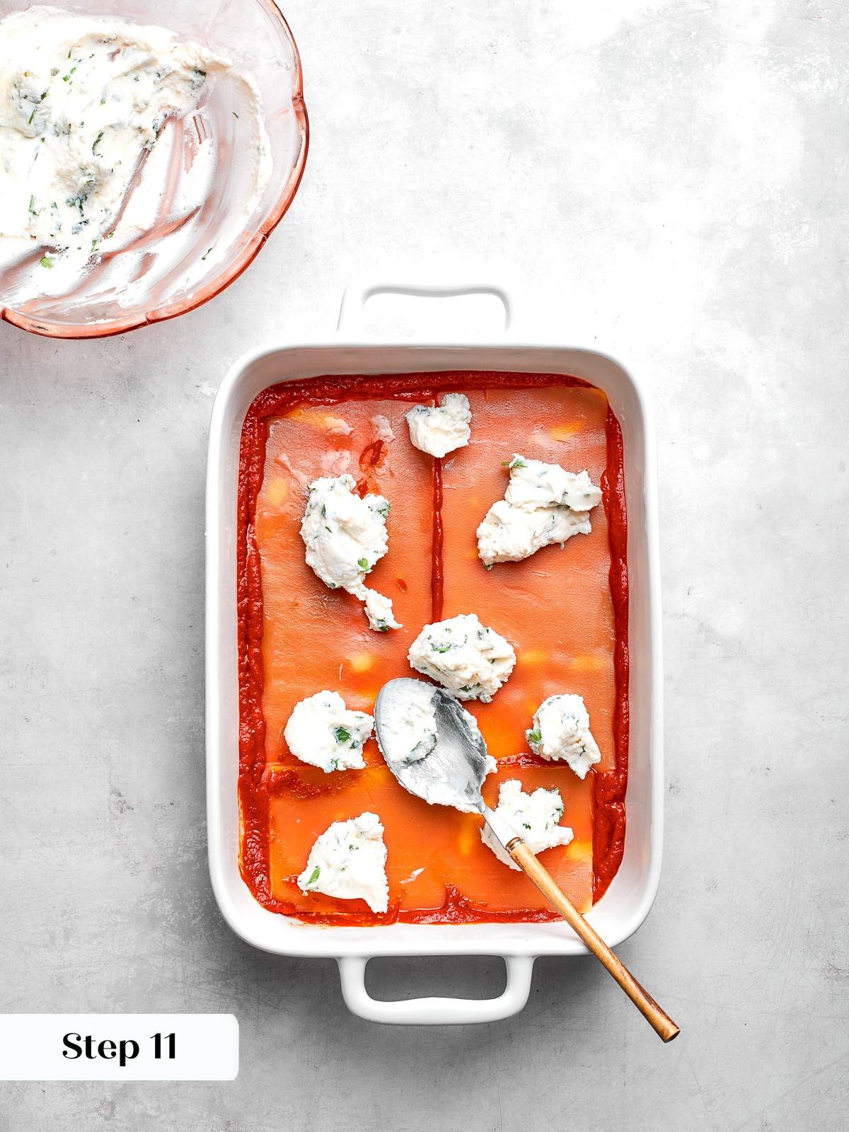 Ricotta mixture being spread evenly over noodles during lasagna layering process.
