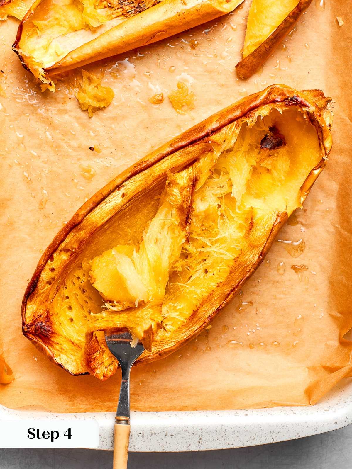 Fork scraping roasted spaghetti squash into strands after baking until tender.