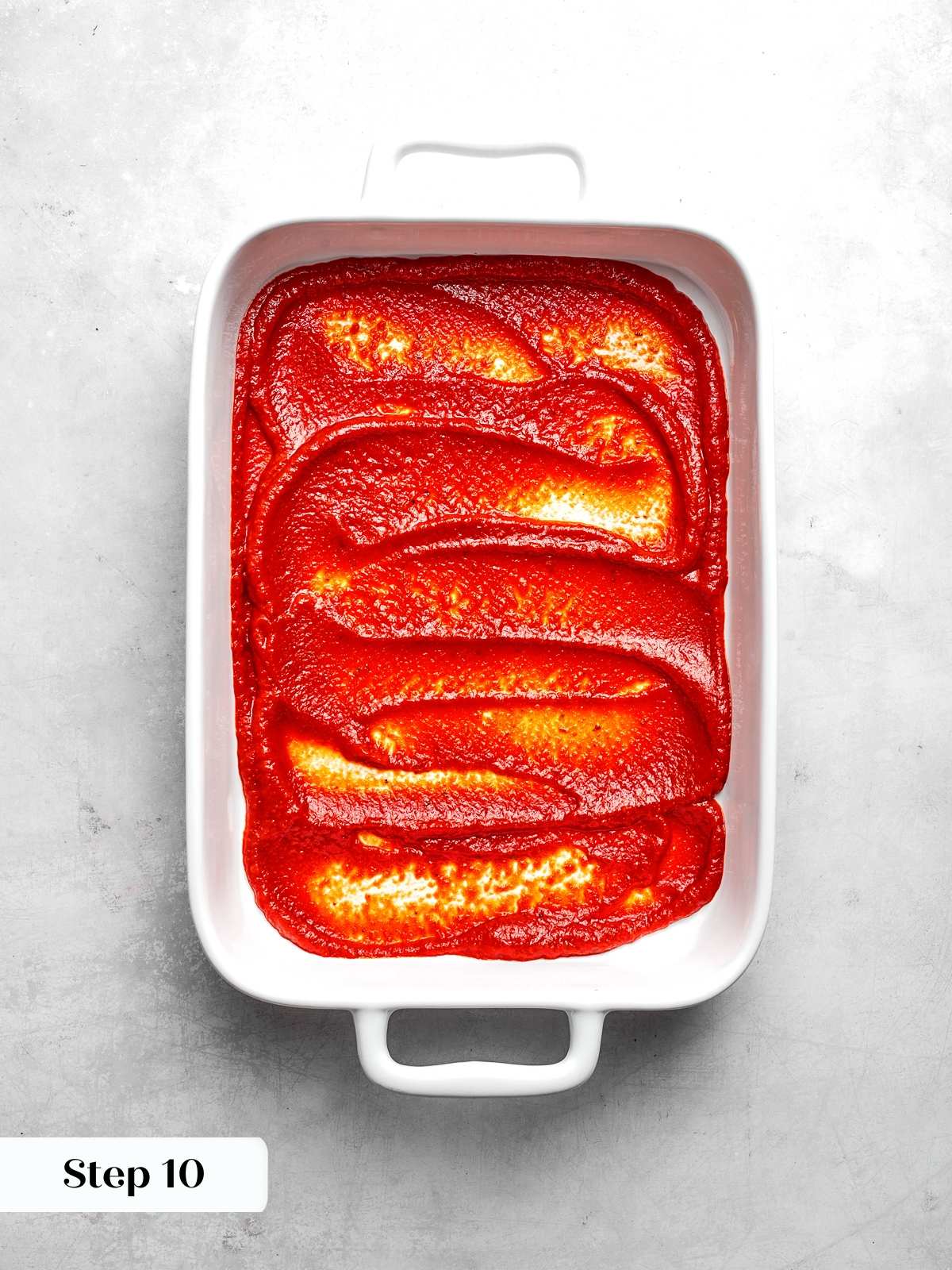 Tomato sauce spread across bottom of baking dish before layering lasagna.