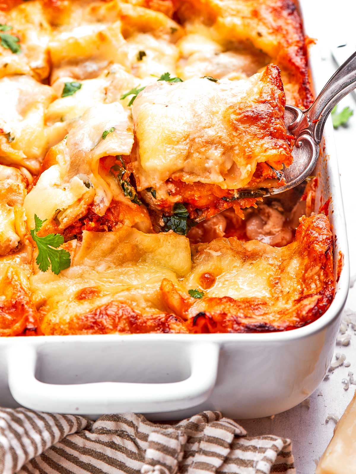 Serving spaghetti squash lasagna from white baking dish with melted cheese and layers.