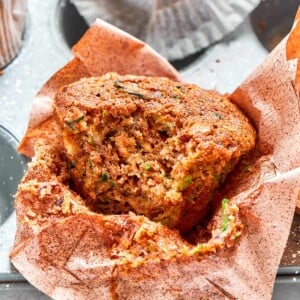 Zucchini muffin with bite taken showing moist crumb and flecks of green zucchini.