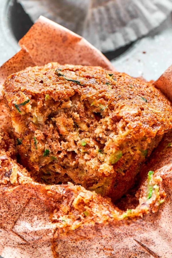 Zucchini muffin with bite taken showing moist crumb and flecks of green zucchini.