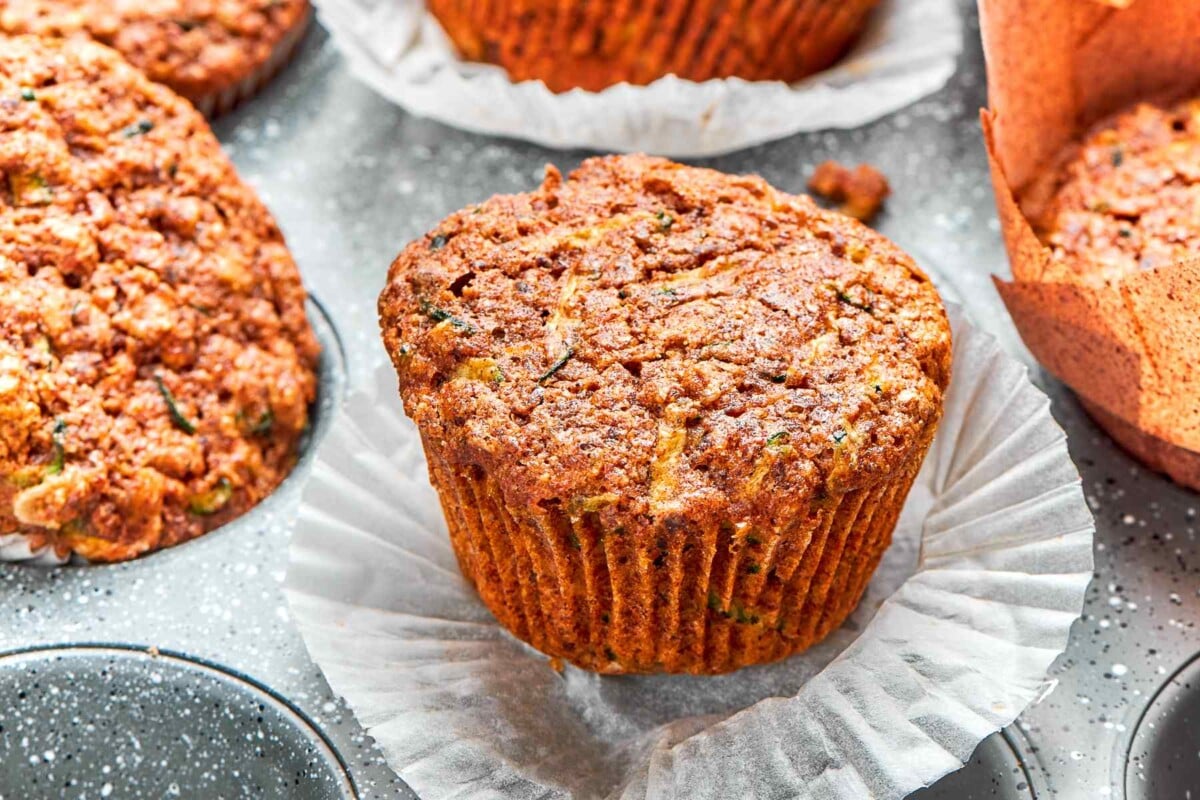 Zucchini muffin with wrapper peeled down revealing moist crumb and flecks of zucchini.