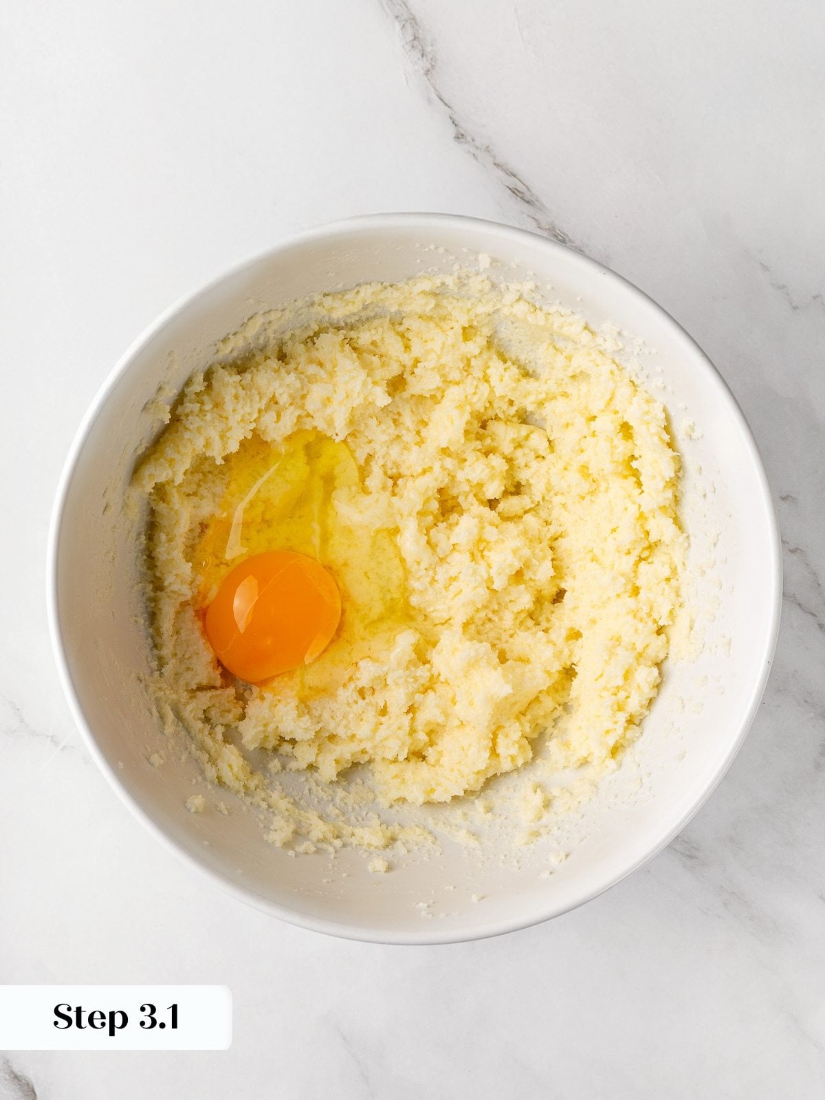 Egg being added to creamed butter and sugar mixture in mixing bowl.