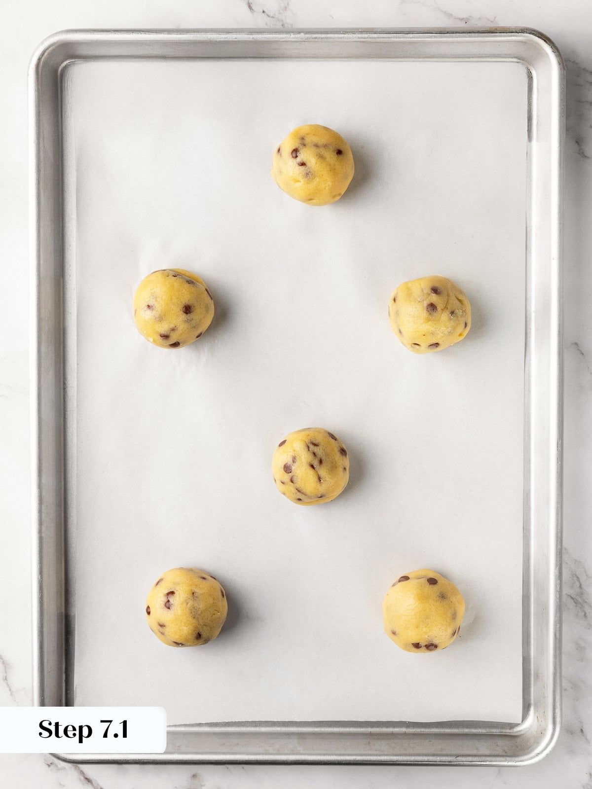 Large cookie dough balls spaced evenly on baking sheet ready for baking.