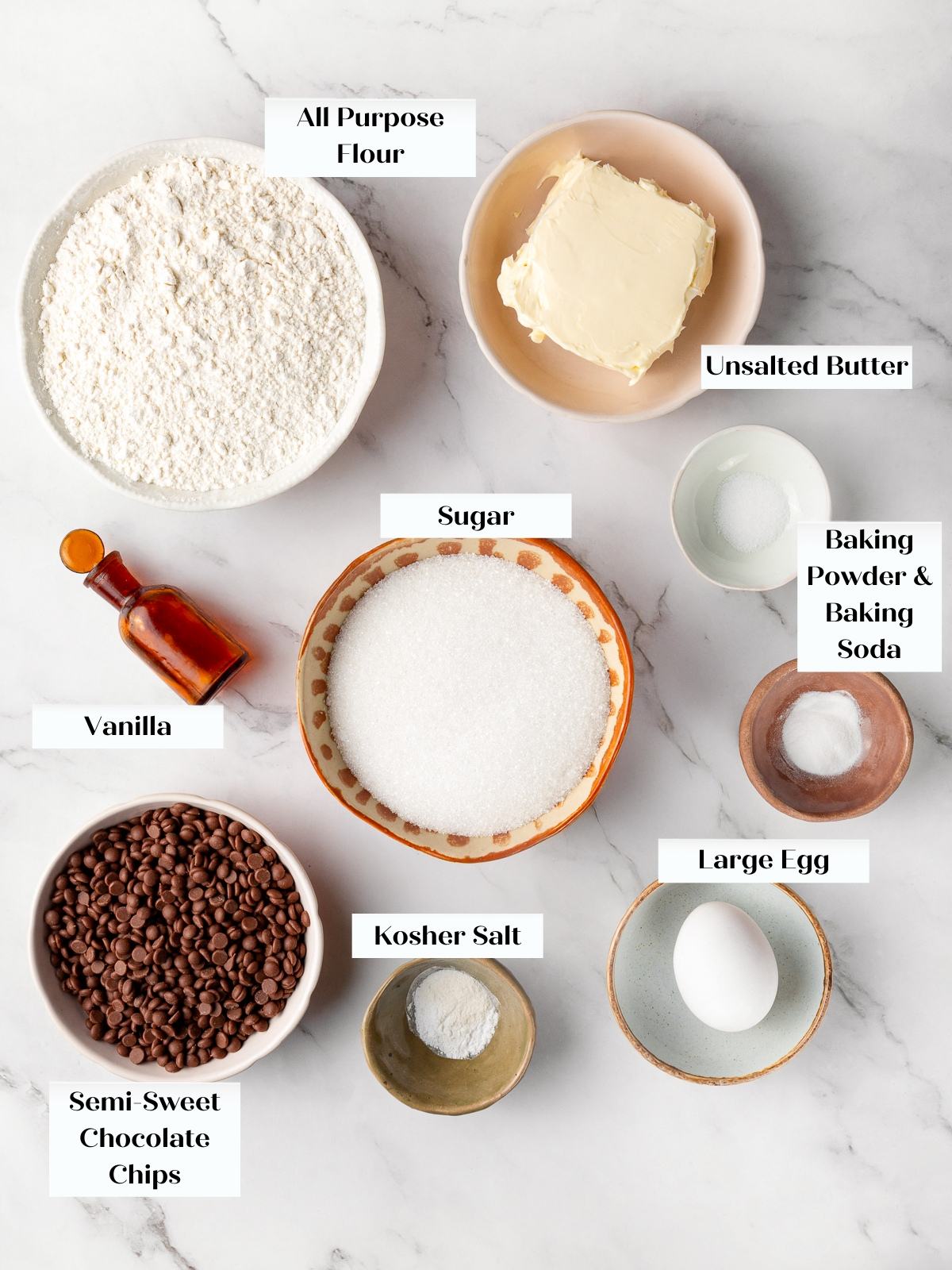 All cookie ingredients arranged on countertop including flour, butter, sugar, and chocolate chips.