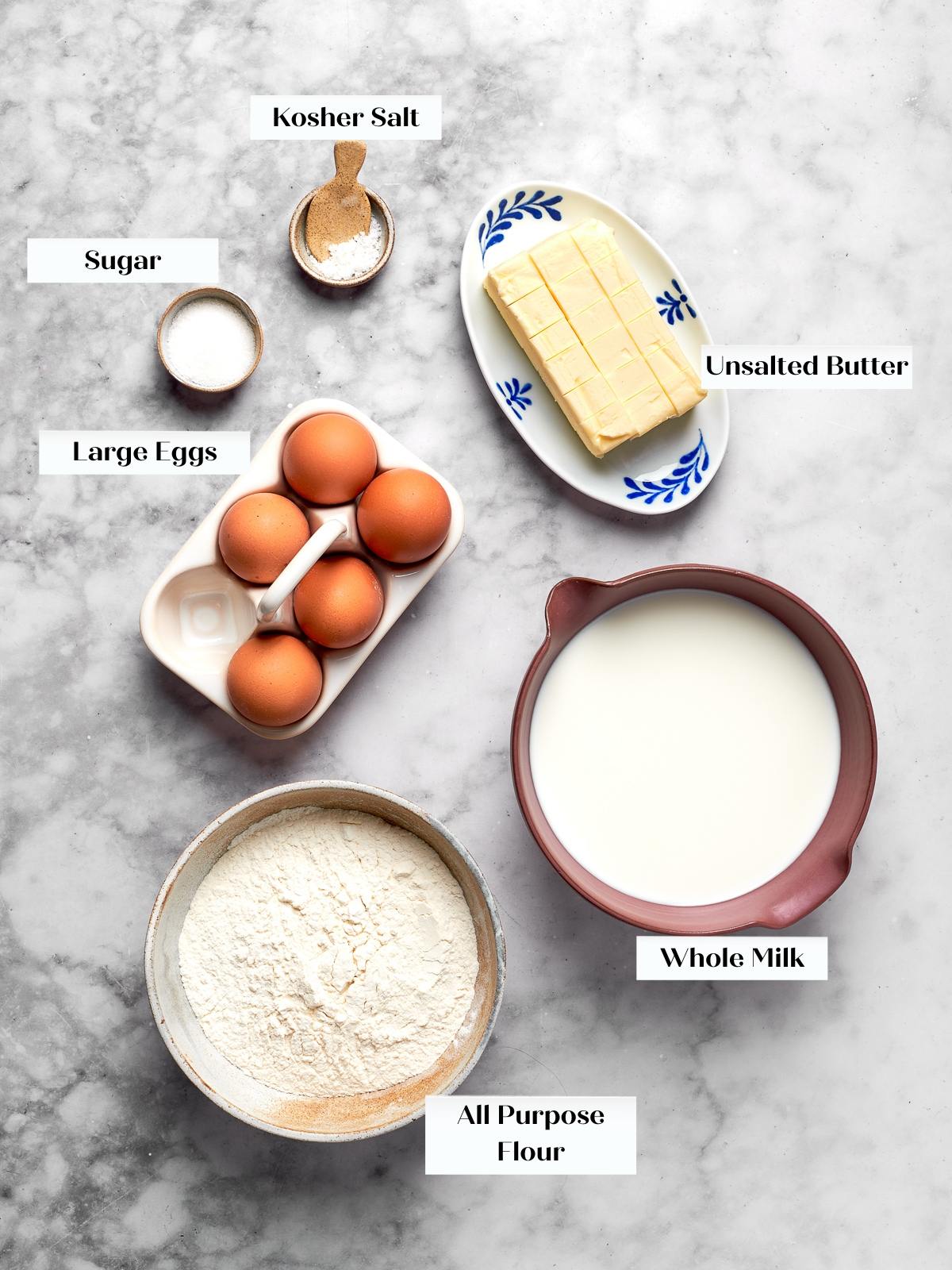 Measured ingredients arranged on countertop including butter, flour, eggs, milk, salt, and sugar.