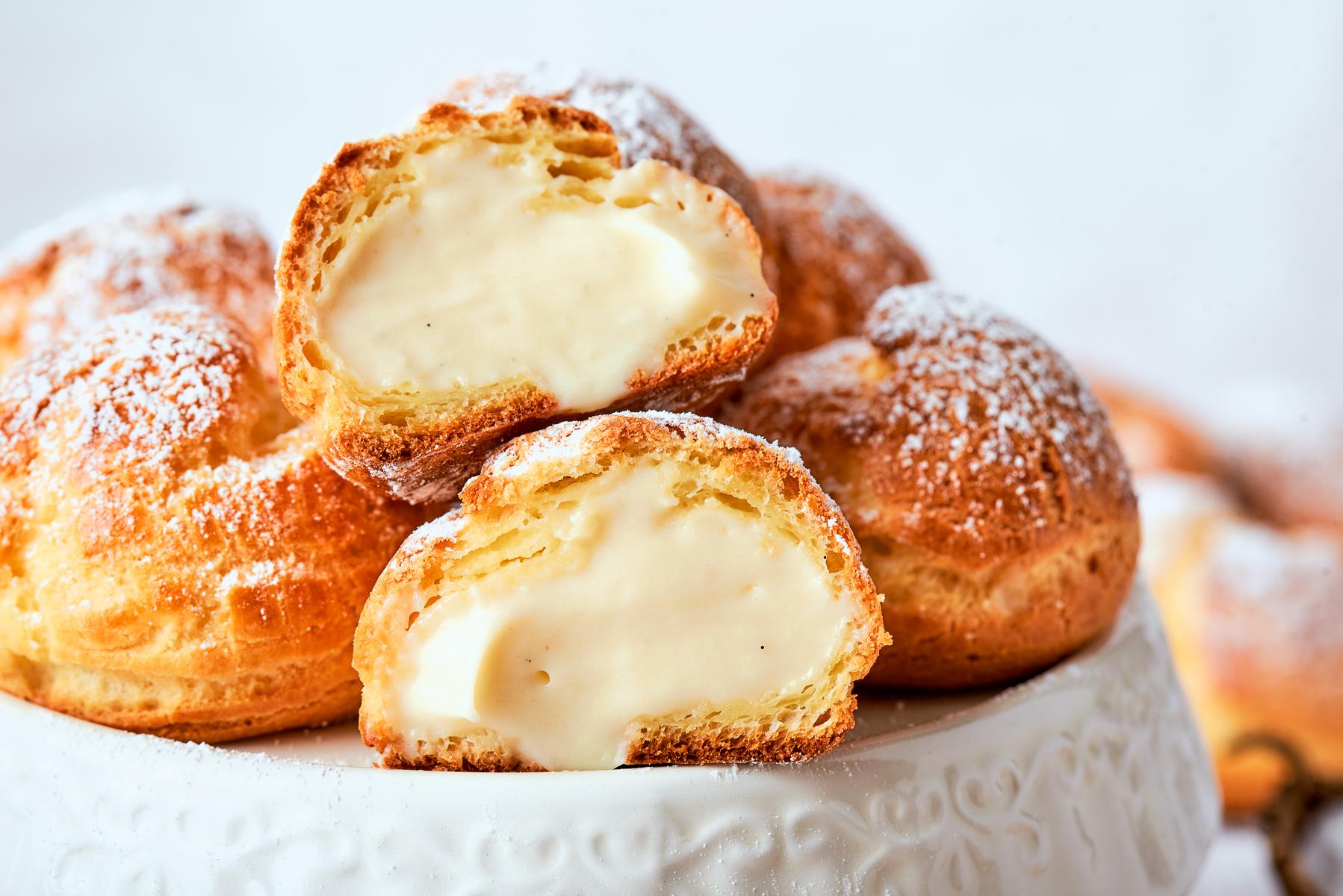Cream puff torn open showing airy hollow shell and soft vanilla cream filling inside.