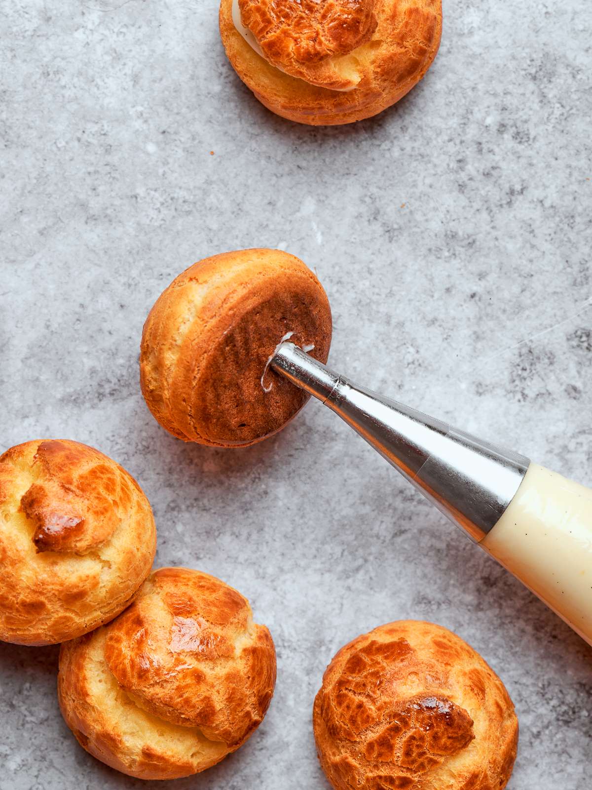 Piping bag filling cream puff shells with silky crème légère through small openings.