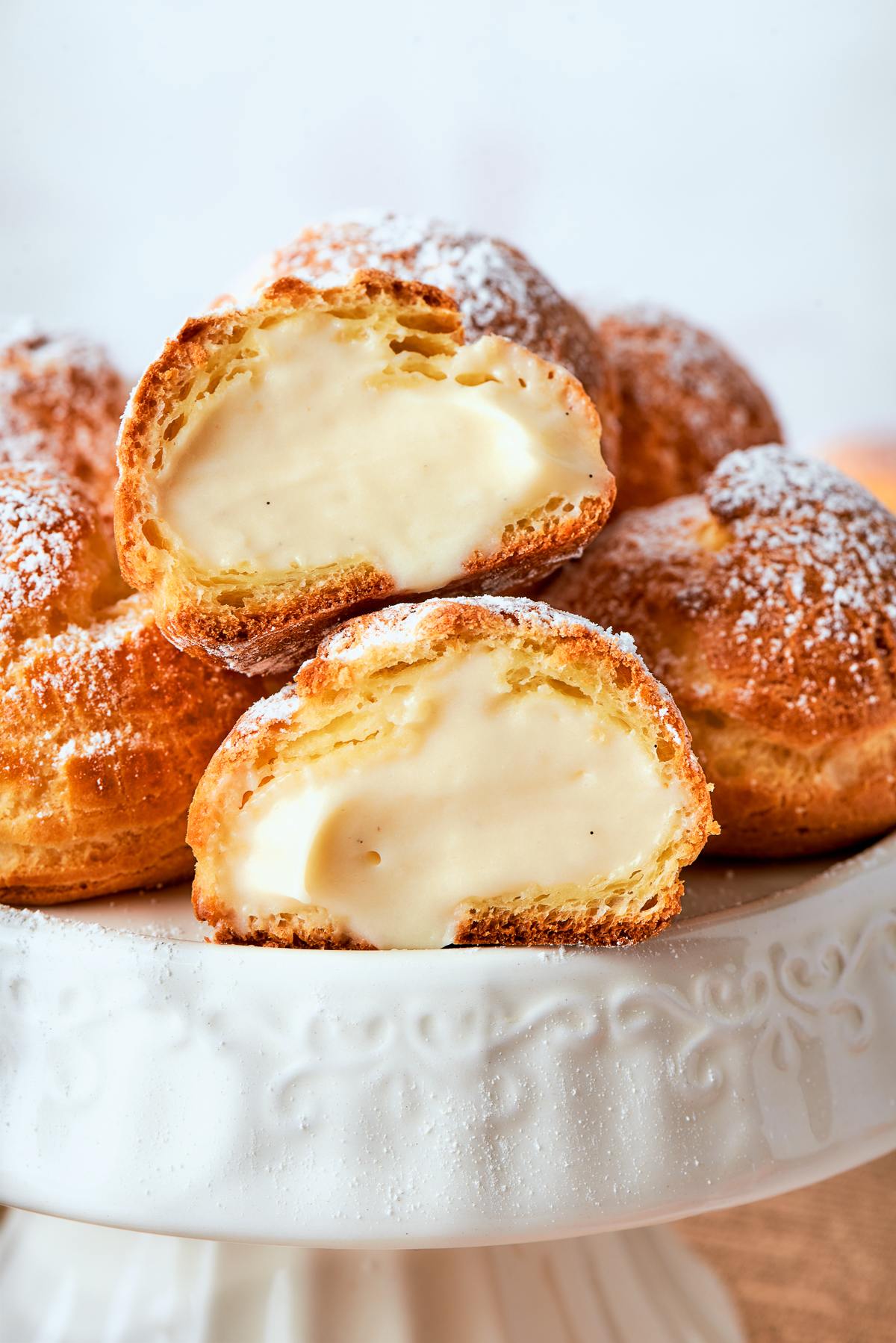 Filled cream puffs displayed on cake stand with light dusting of powdered sugar.