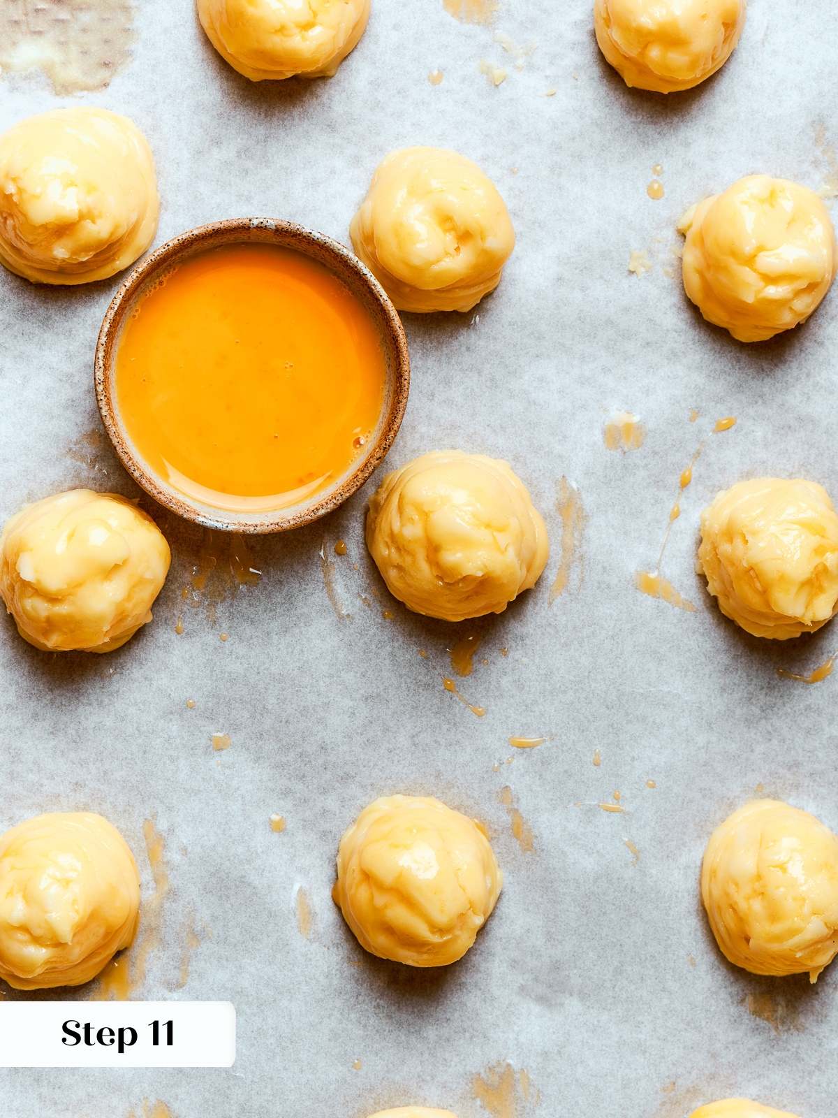 Egg wash brushed over piped gougères smoothing tops and preparing for baking.