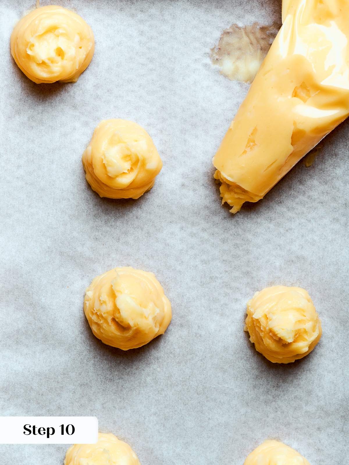 Choux dough piped into small rounds on parchment with consistent spacing between each.