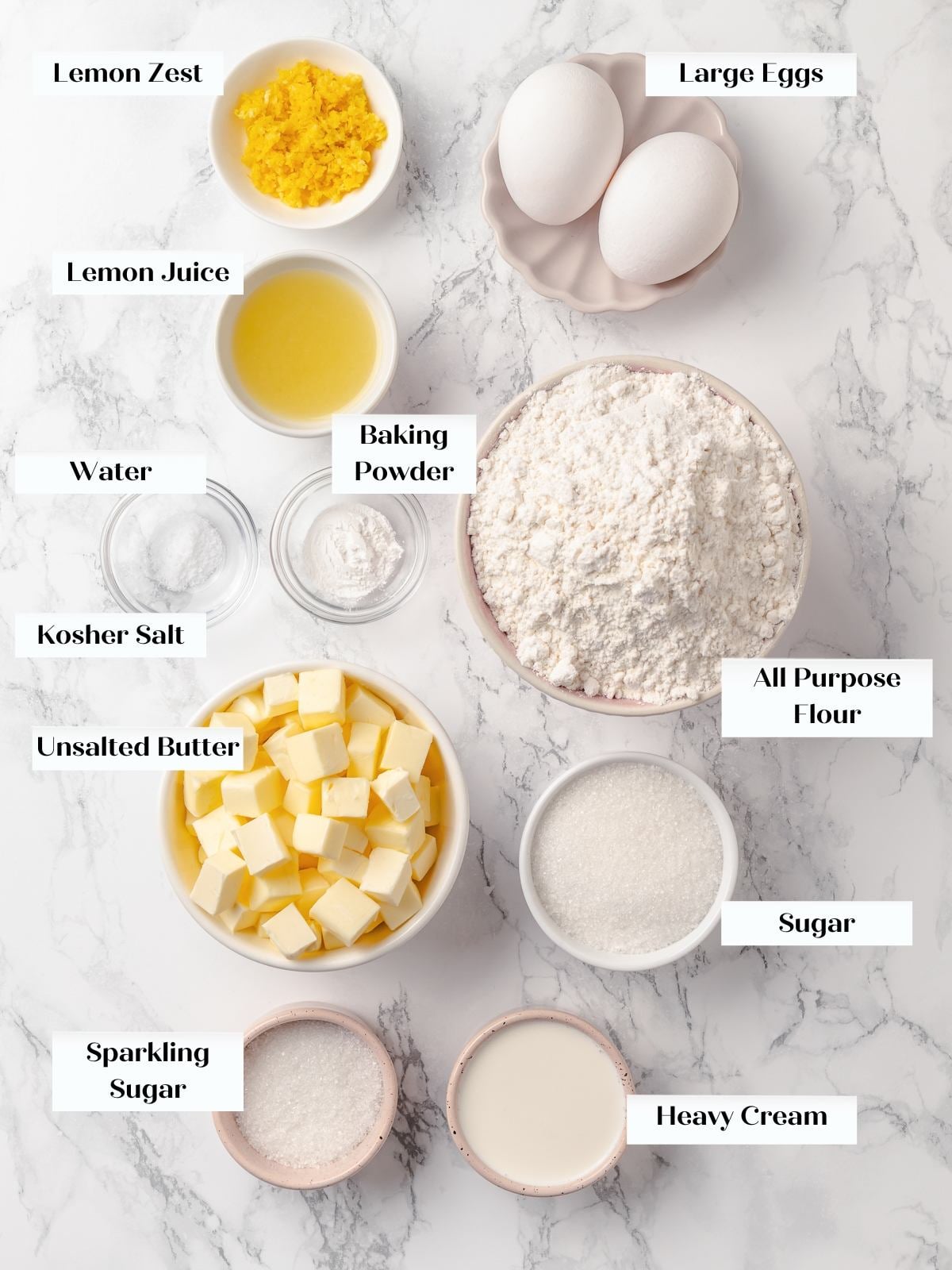 Ingredients for lemon scones arranged on countertop including flour, butter, eggs, and lemons.