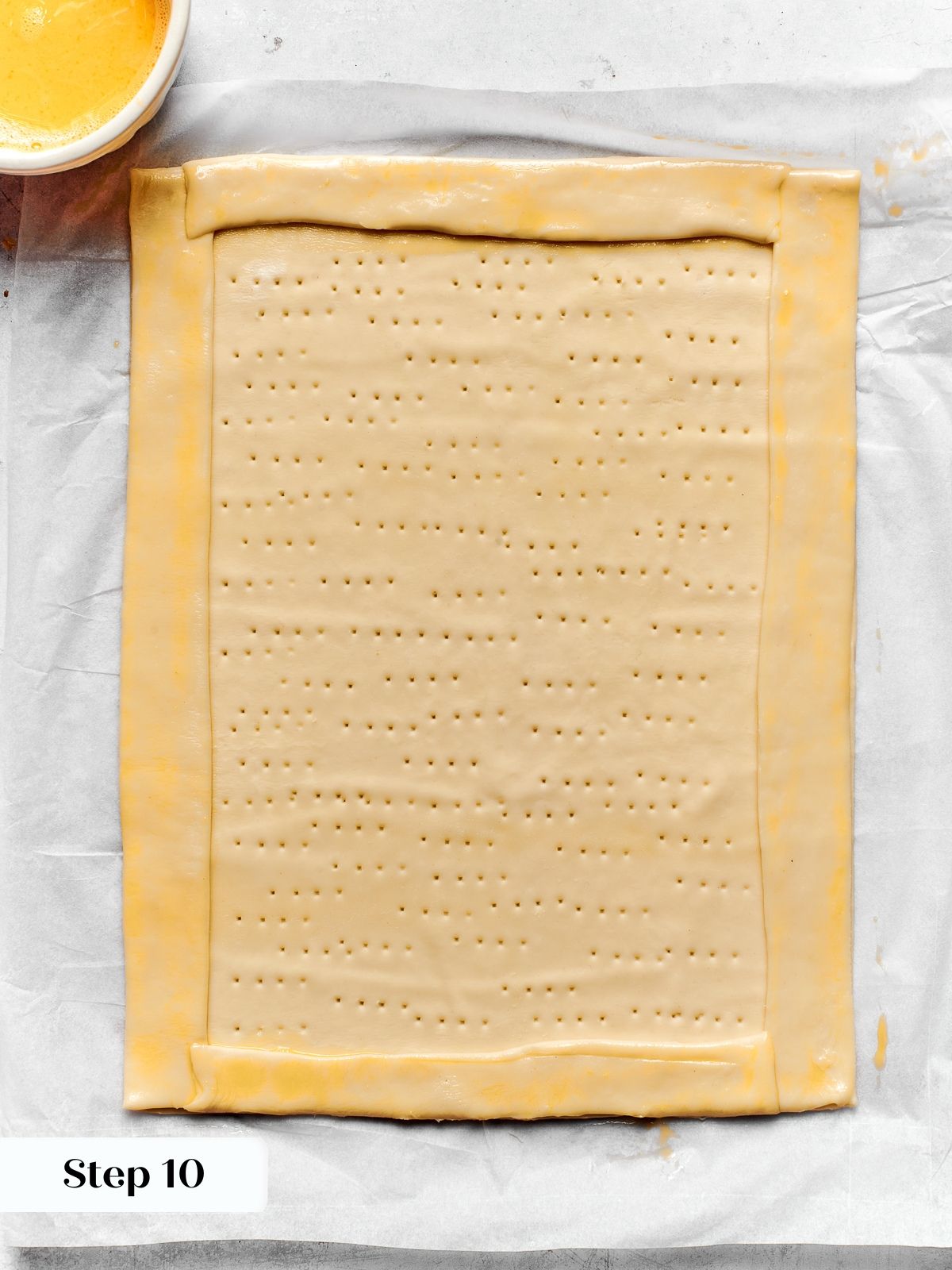 Puff pastry base with border attached and evenly docked using fork before baking.