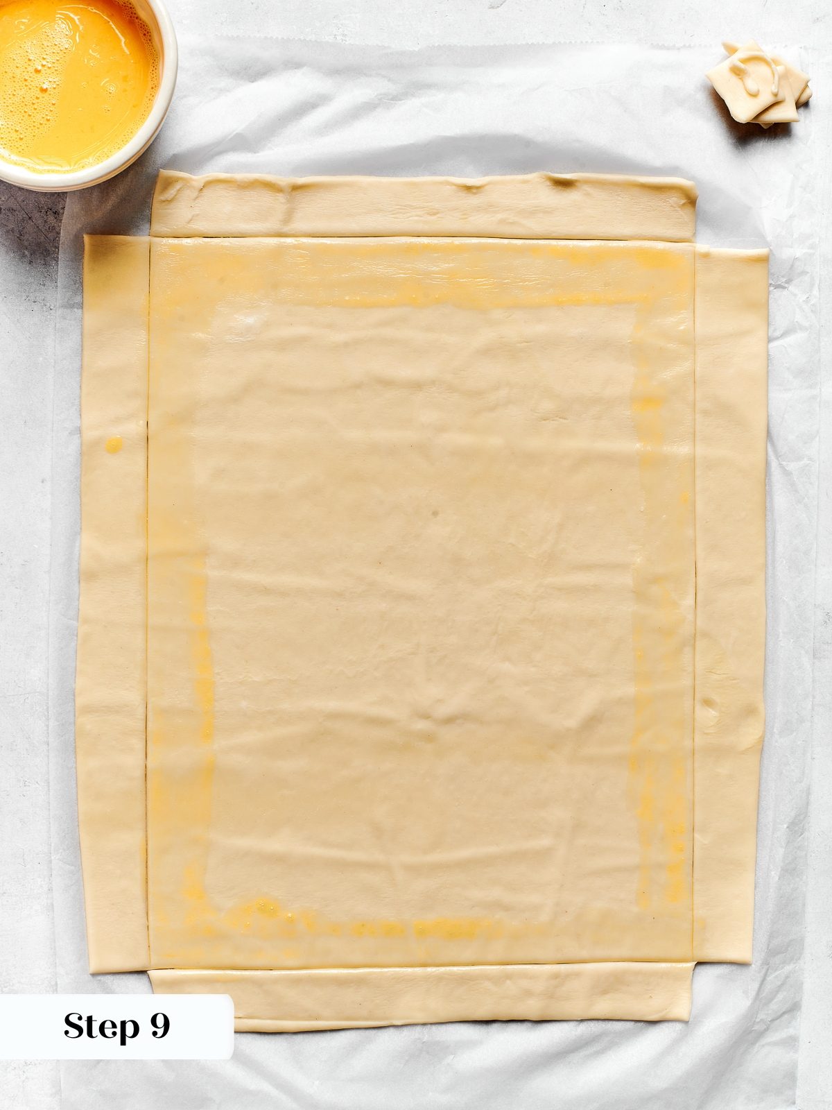 Egg wash applied along pastry edges to attach border strips securely before baking.