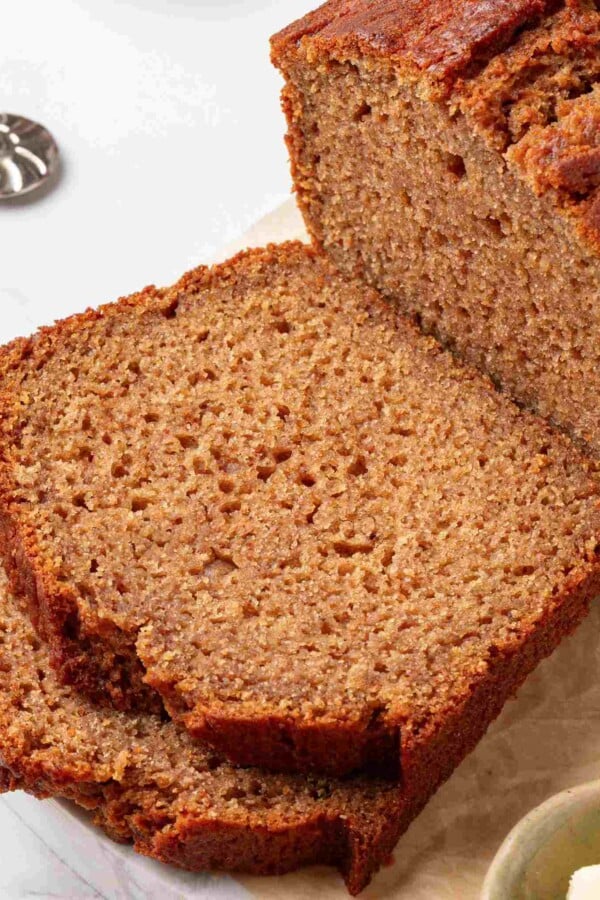 Tight square framing of the cut loaf and two slices showing tender cinnamon-flecked crumb in detail.