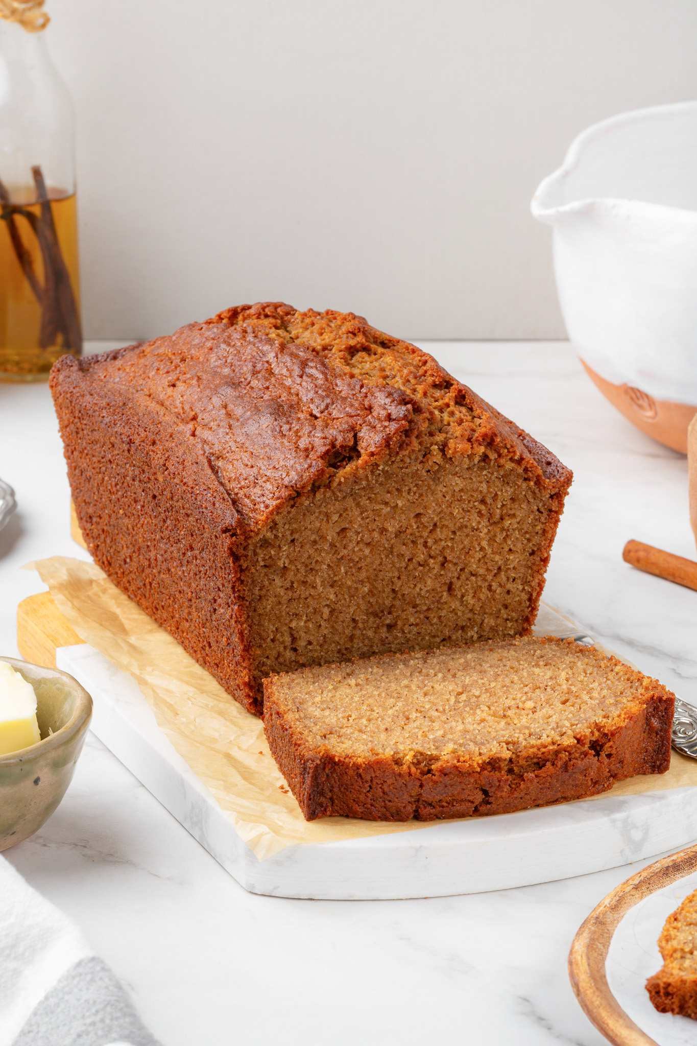 Tall caramelized loaf with a single freshly cut slice resting on parchment-lined wood and marble.