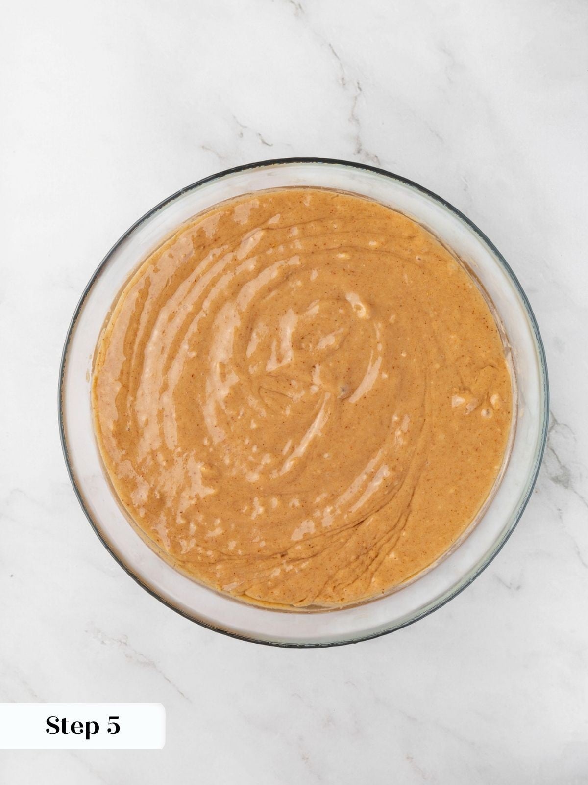 Smooth glossy batter swirled into a uniform pale orange after the warm coconut oil is added.
