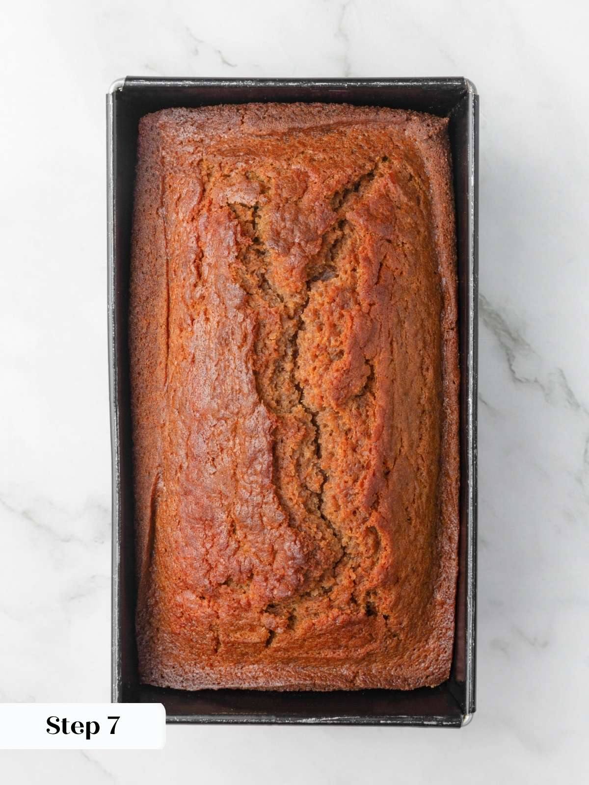 Deeply golden baked loaf with a cracked center crust still resting in its metal loaf pan.